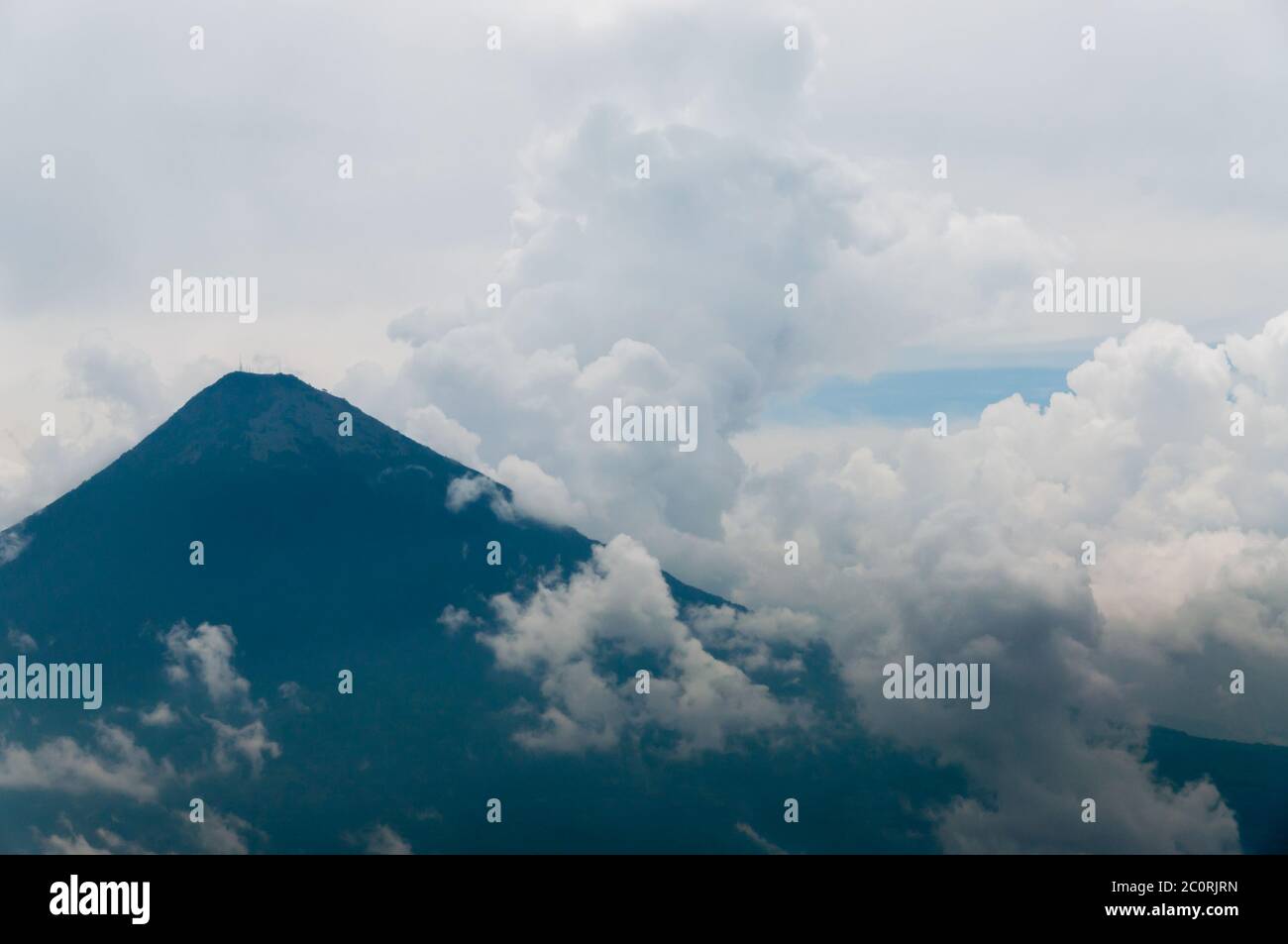 Grande cima del vulcano circondato dalla nebbia e dense nubi su campo verde Foto Stock