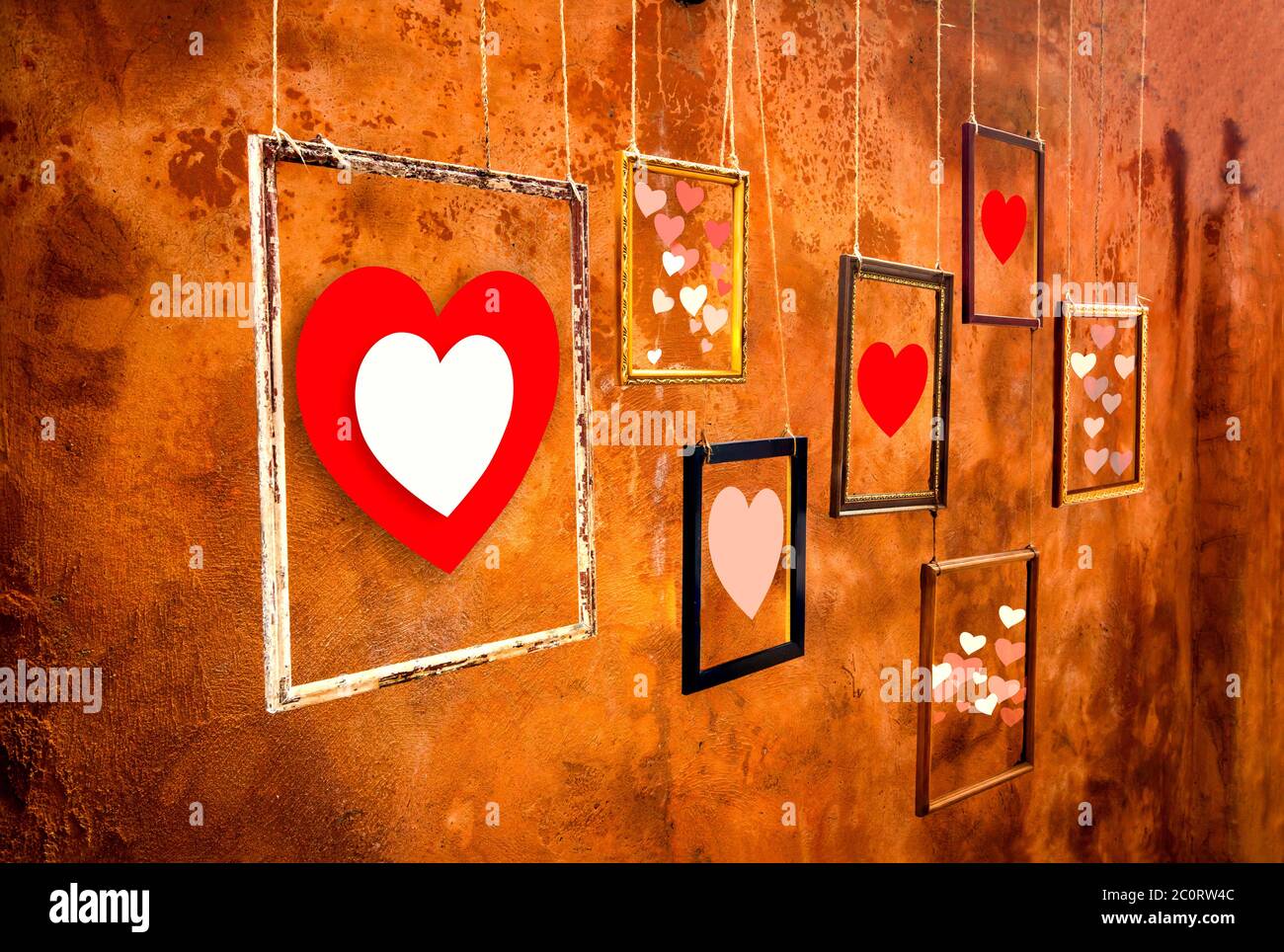 Cuori in vecchie cornici e appesi al vecchio sfondo arancione della parete, mostrando il vostro concetto di giorno Amore e San Valentino Foto Stock