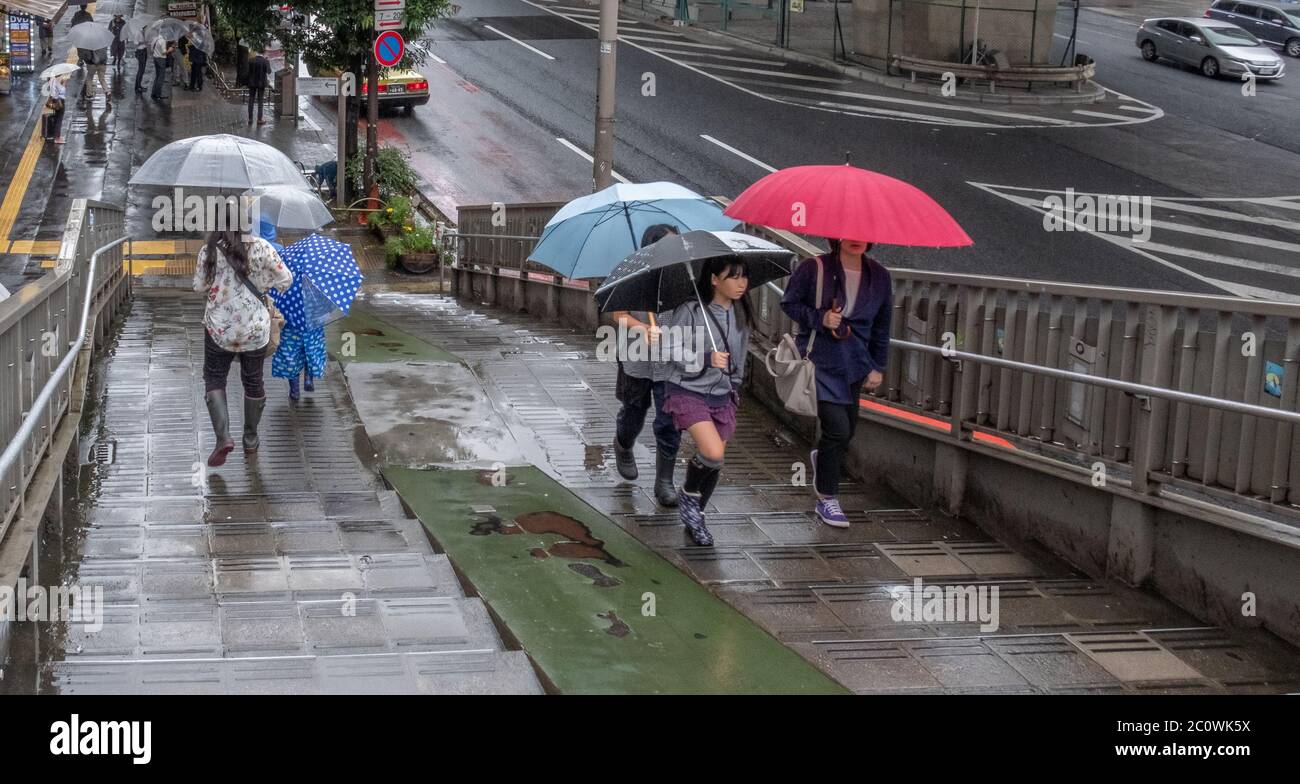 Folla pedonale al ponte pedonale oltrepassa le scale durante una giornata piovosa con ombrello a Shibuya, Tokyo, Giappone Foto Stock