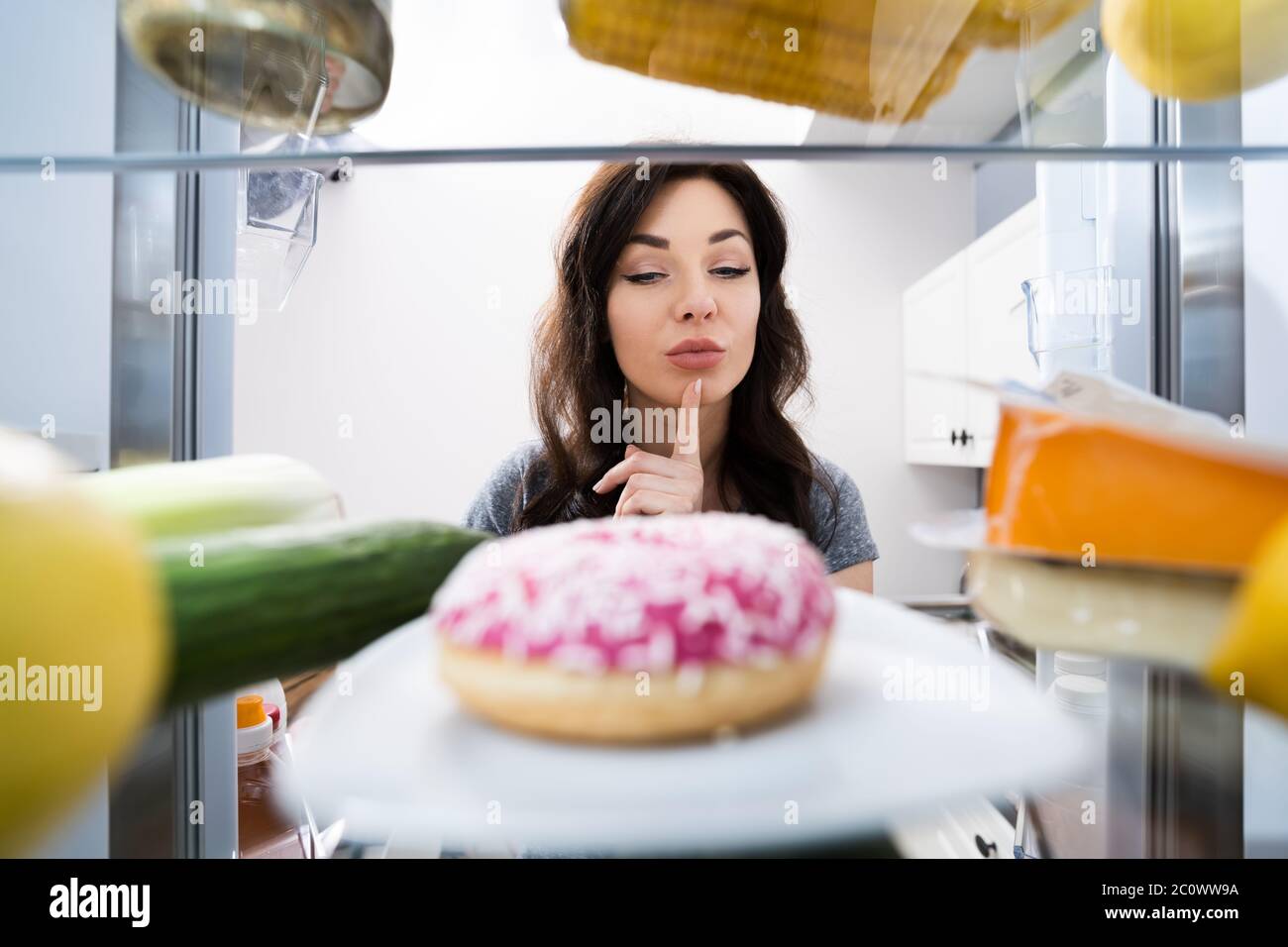 Donna confusa pensando a dolci in frigorifero o frigorifero Foto Stock