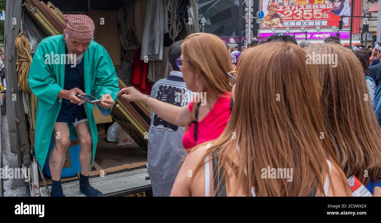 Vecchio giapponese che tiene uno smartphone con turisti stranieri a Shibuya, Tokyo, Giappone Foto Stock