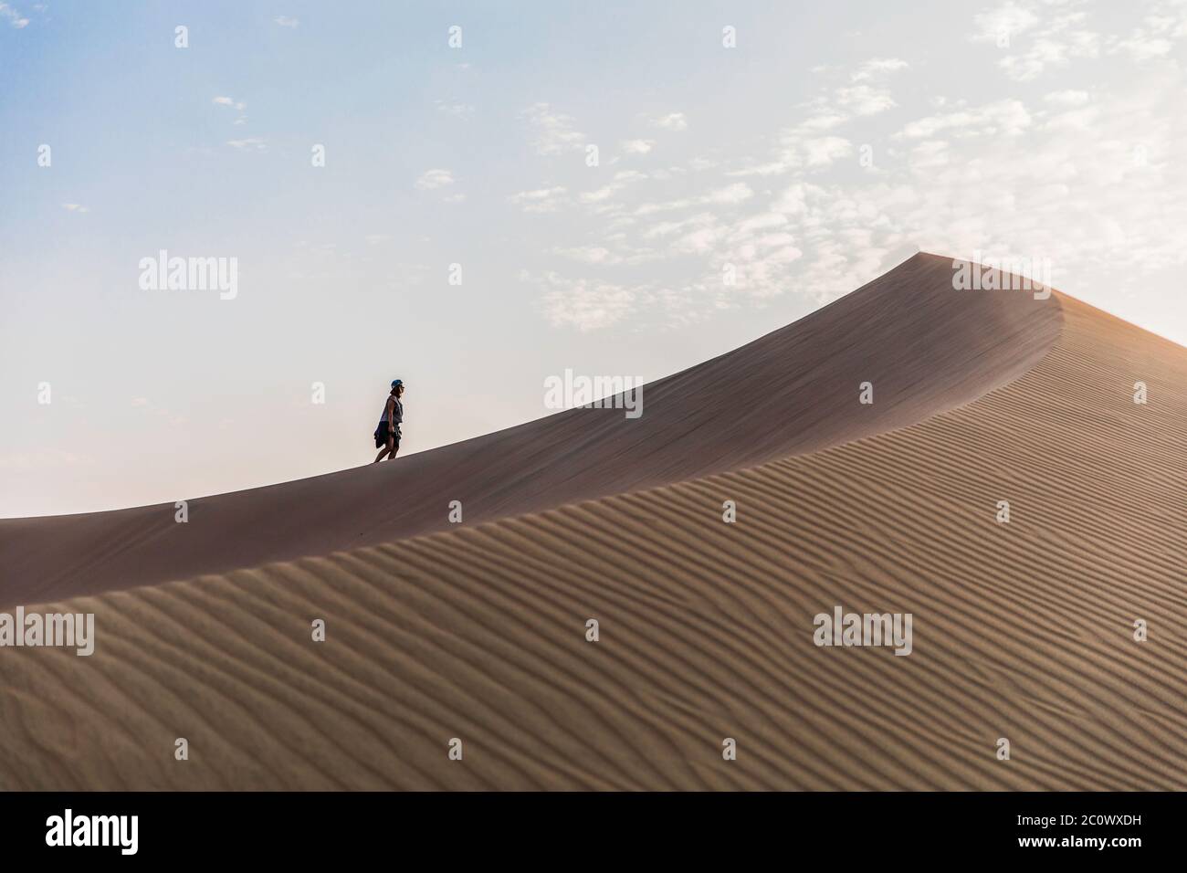 donna che cammina fino alla cima di una duna nel mezzo del deserto e delle nuvole Foto Stock