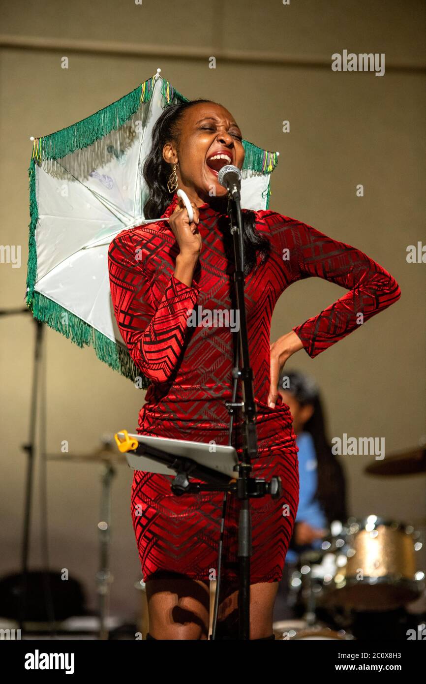 Una cantante jazz afro-americana entusiasta tiene un parasolo mentre si esibisce durante una celebrazione notturna di Mardi Gras a Costa Mesa, CA. Foto Stock