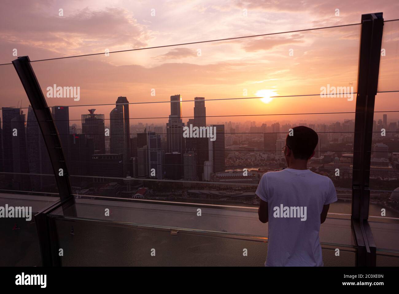 Giovane uomo che osserva il tramonto sullo skyline del centro di Singapore, visto da Marina Bay Sands. Singapore Foto Stock