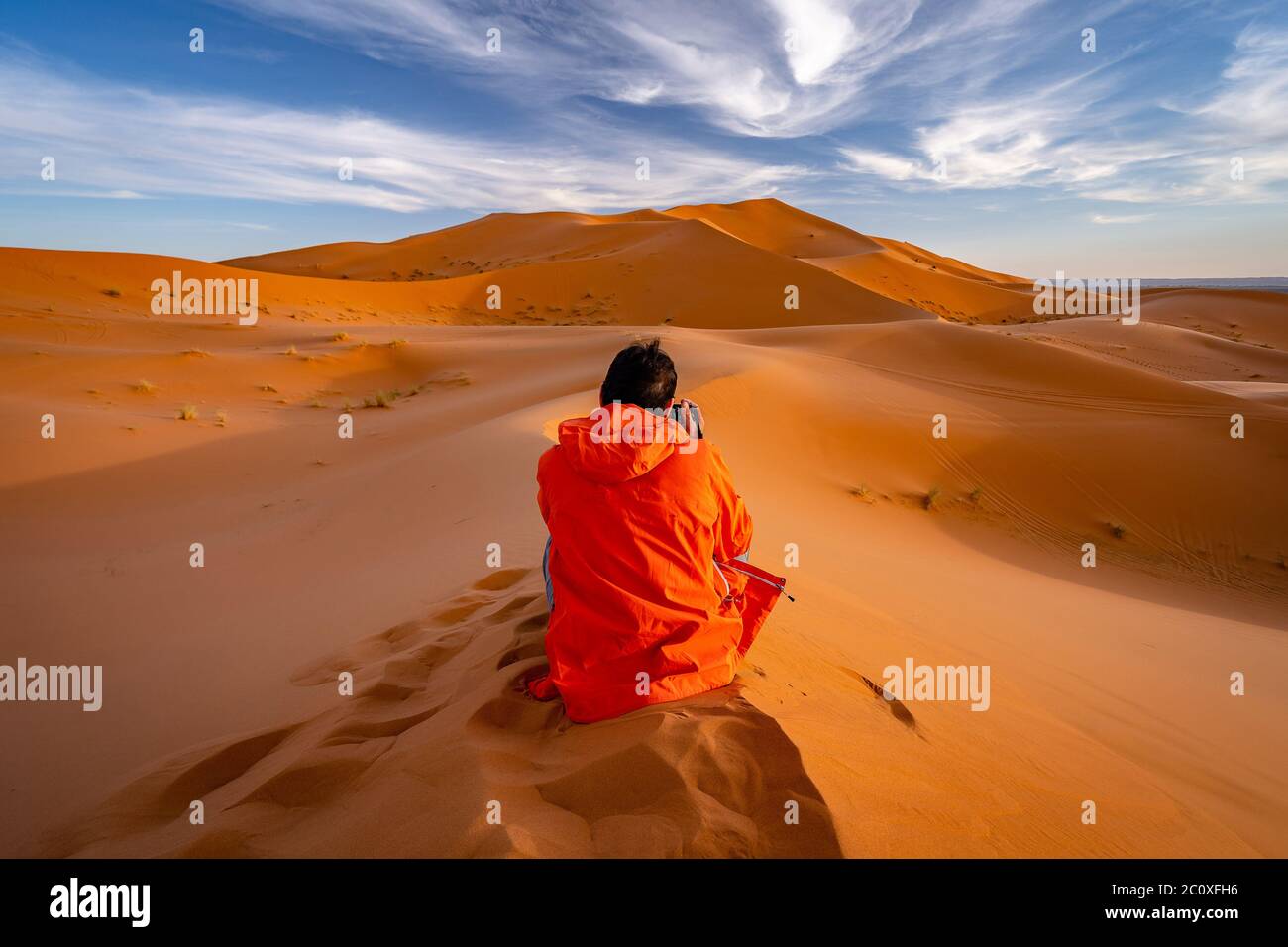 Una persona che si siede in cima alle dune di sabbia e scatta foto del deserto del Sahara in Marocco Foto Stock