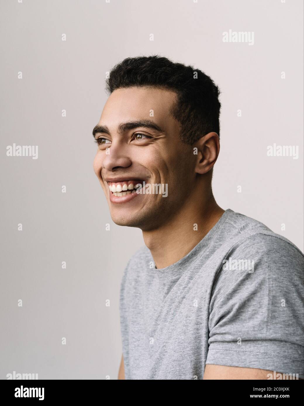 Ritratto di bell'uomo afroamericano sorridente con felice volto emozionale, con t-shirt casual grigia. Modello di moda positivo che posa per le immagini Foto Stock