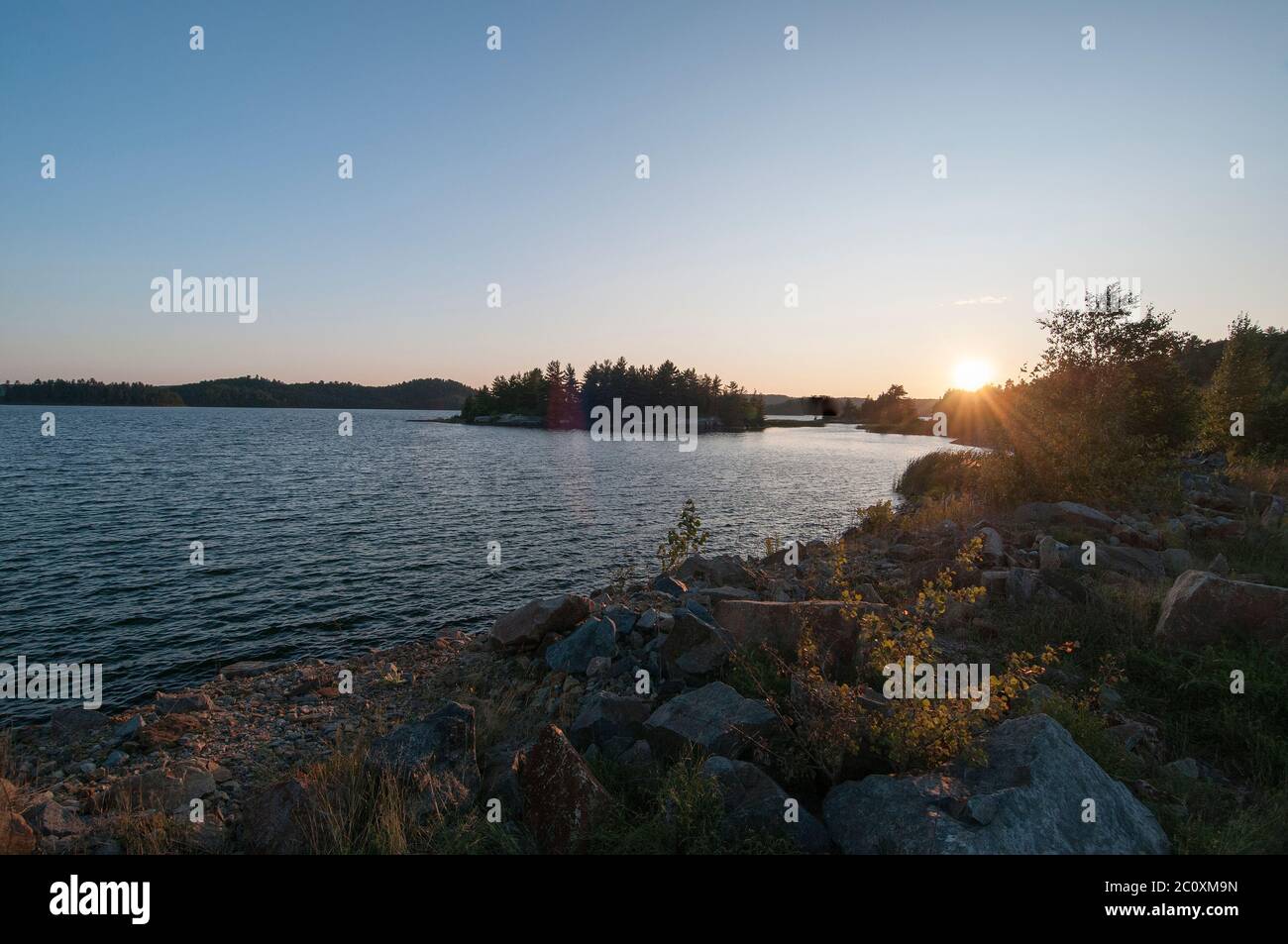Scenario estivo con tramonto all'orizzonte con acqua e rocce lungo la costa che mostra la sua stagione estiva. Foto Stock