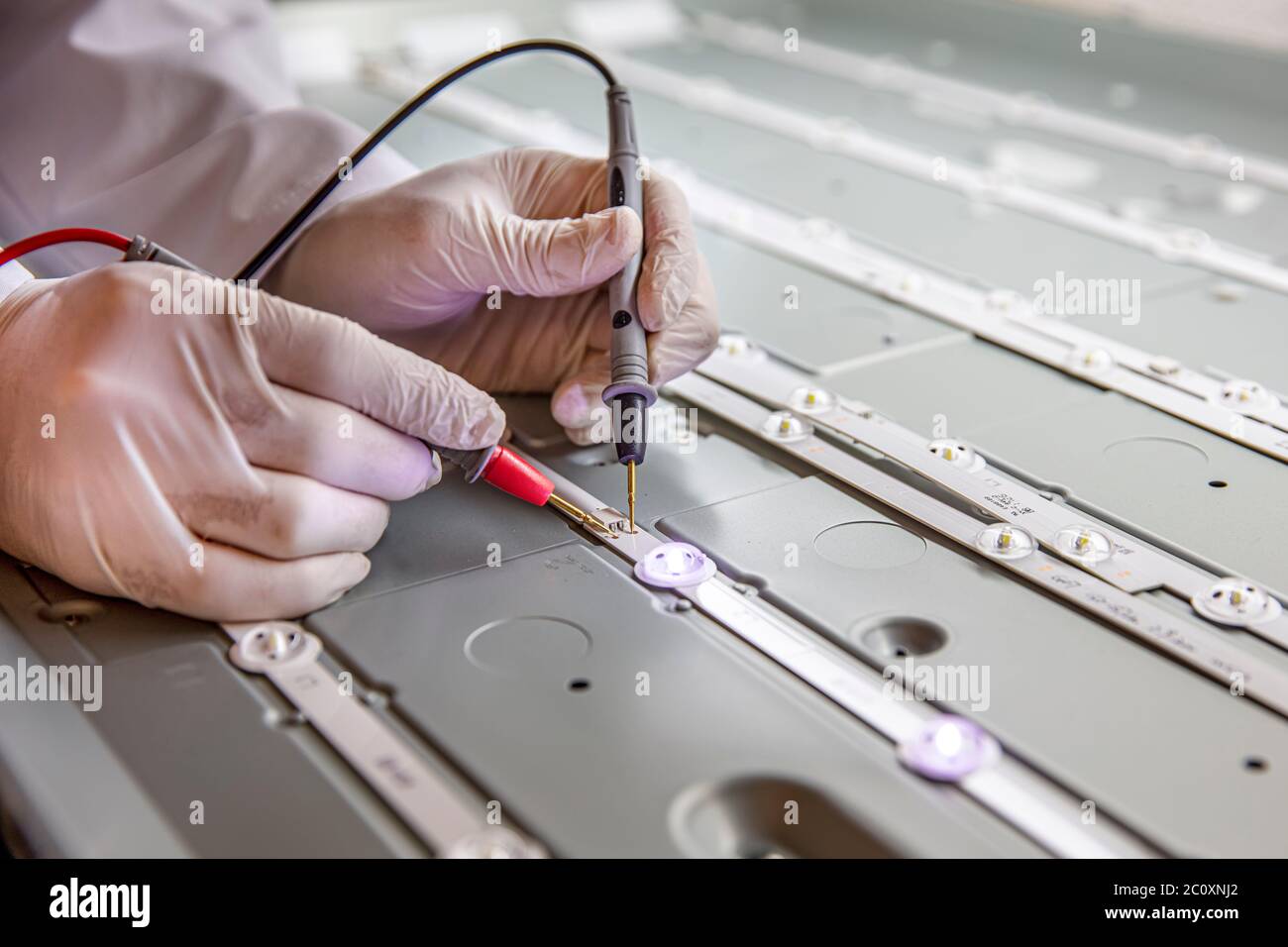 Riparazione di televisori LED con multimetro digitale, controllo di strisce LED. Il tecnico misura la tensione sulla scheda LED con un multimetro. Riparare Foto Stock