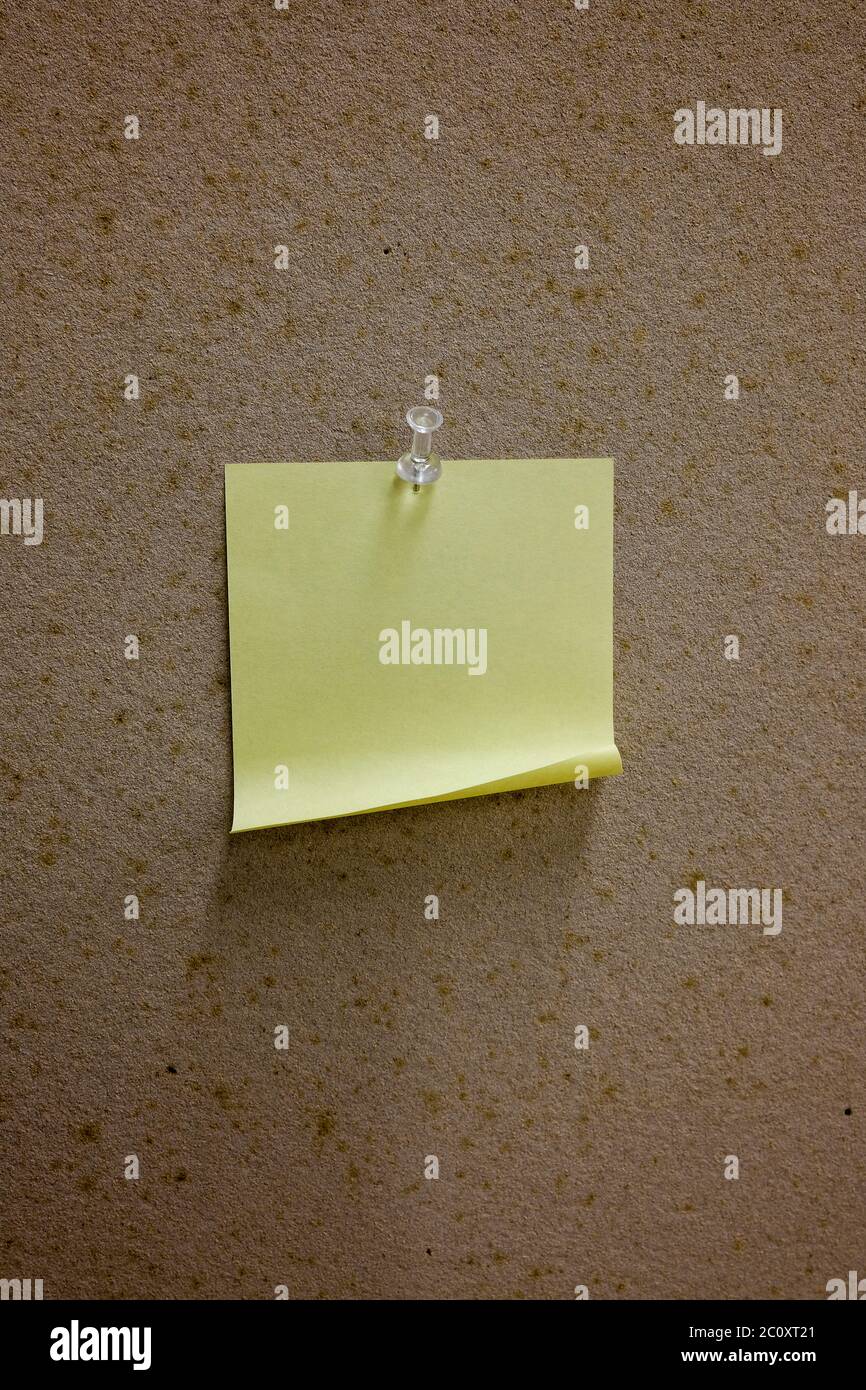Una nota gialla vuota su una bacheca con un pin Foto Stock
