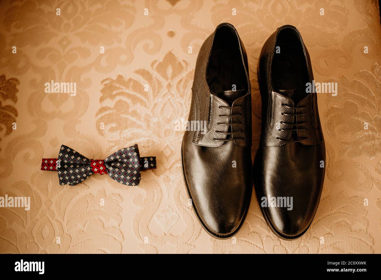 Primo piano degli accessori moderni per lo sposo. Viscere nere, scarpe in pelle e fiore boutonniere su sfondo rustico. Set per uno stile formale di indossare Foto Stock