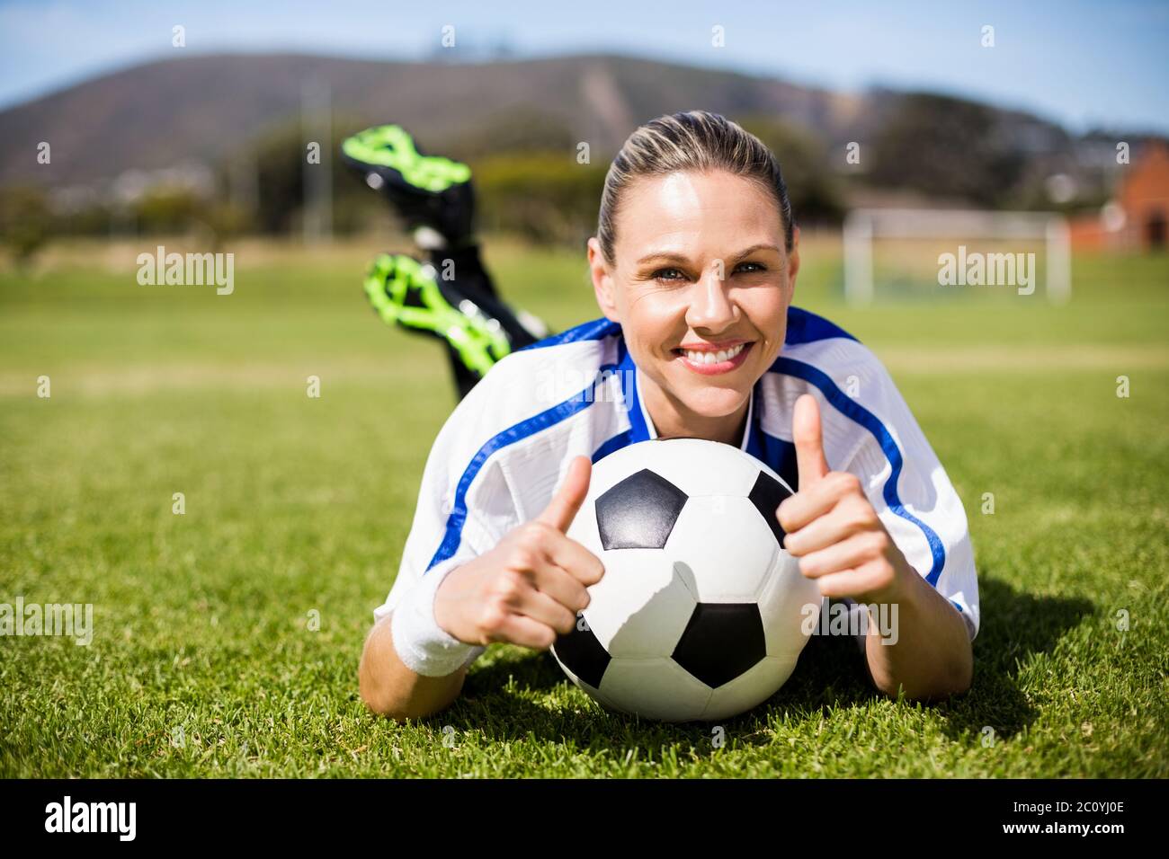 Ritratto femminile di giocatore di football giacente su di un campo da calcio e mostrando il suo pollice Foto Stock