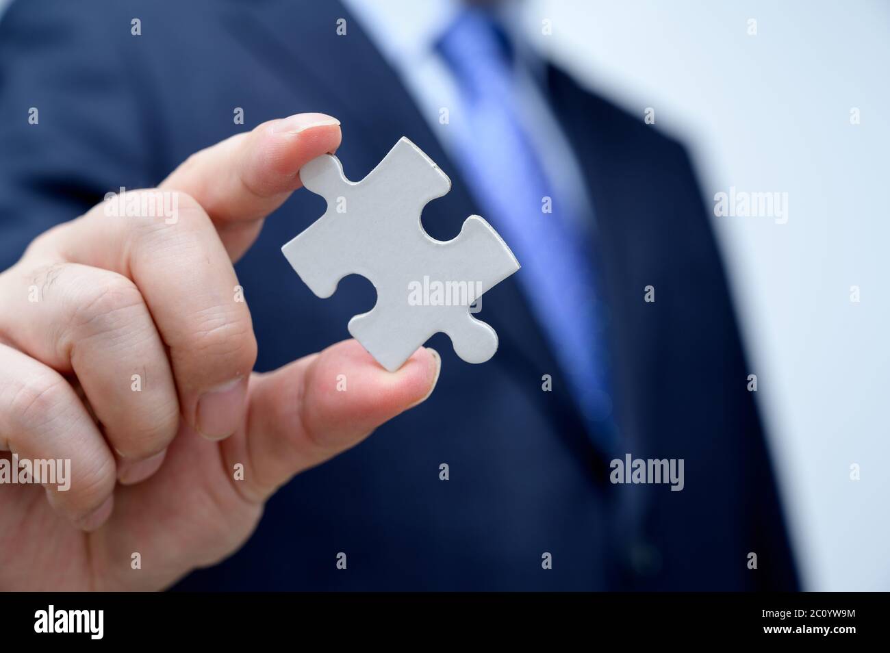 Uomo d'affari che mostra un pezzo di puzzle jigsaw. Concetto di lavoro e lavoro di squadra. Foto Stock Uomo d'affari che mostra un pezzo di puzzle jigsaw. Concetto di lavoro e lavoro di squadra. Foto Stock