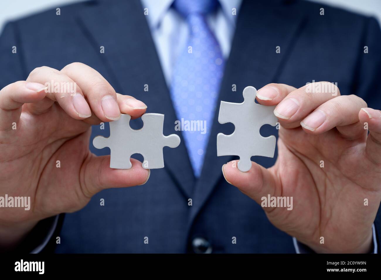 Uomo d'affari che mostra un pezzo di puzzle jigsaw. Concetto di lavoro e lavoro di squadra. Foto Stock Uomo d'affari che mostra un pezzo di puzzle jigsaw. Concetto di lavoro e lavoro di squadra. Foto Stock
