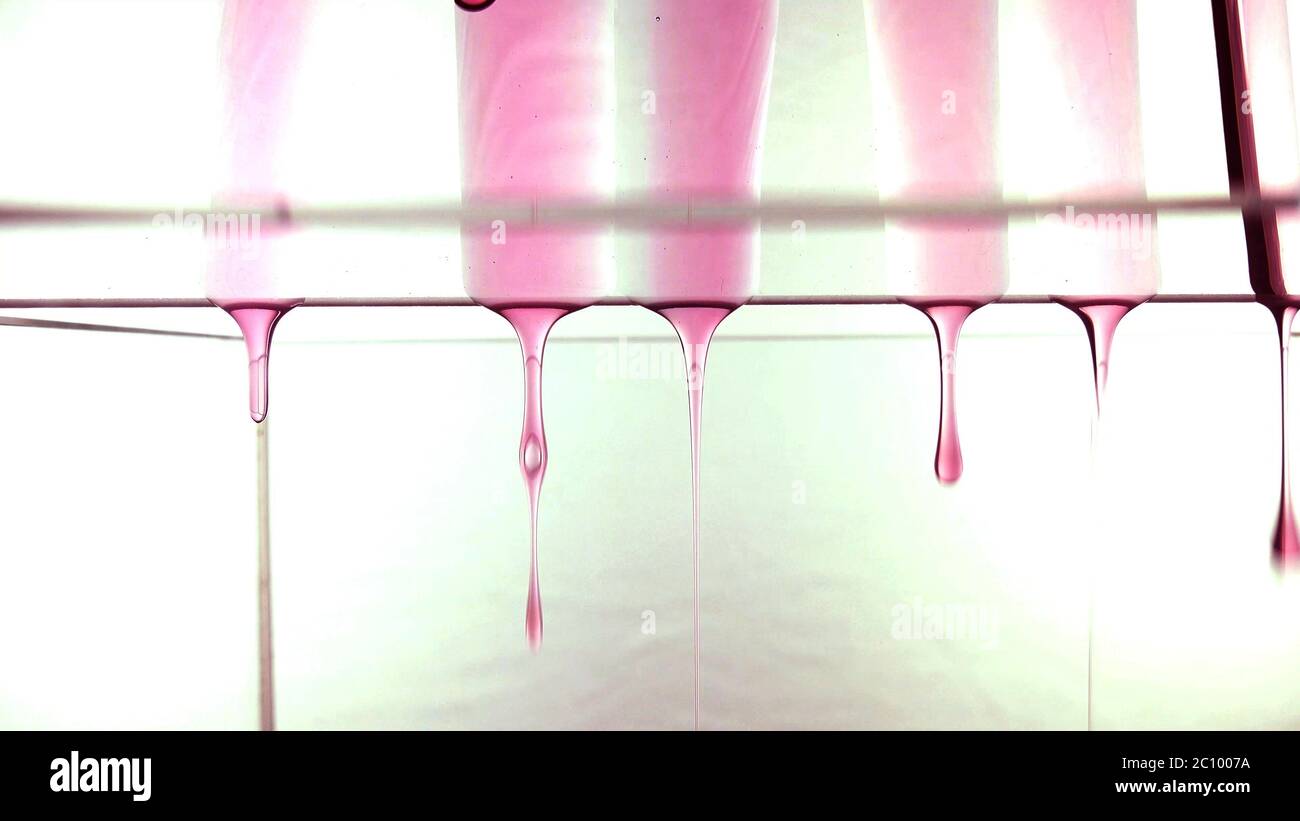 Gocciolamento lento di gocce rosse trasparenti sulla superficie di vetro. Foto Stock