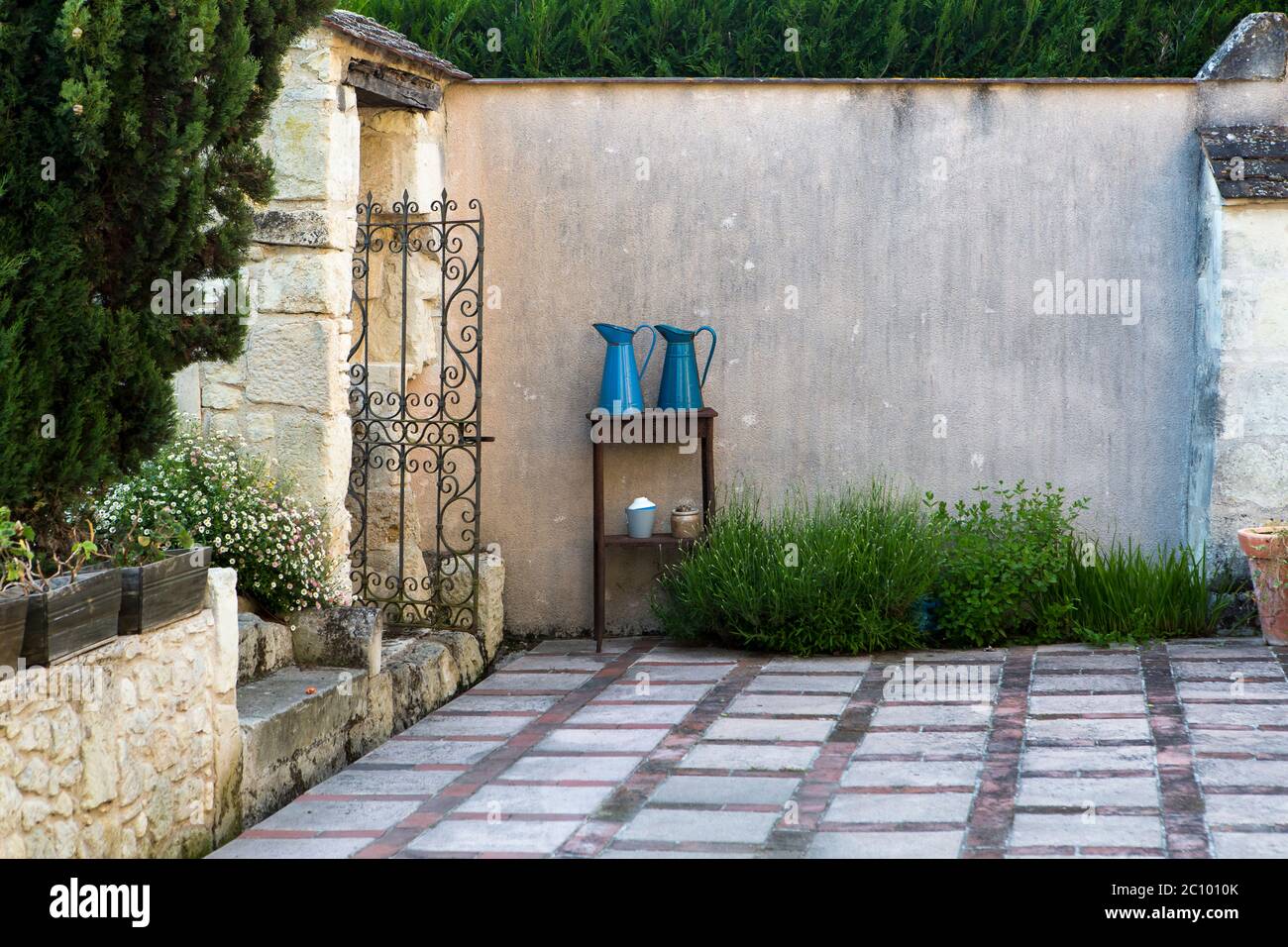 Cortile tradizionale francese giardino con pavimenti decorativi patio, piante, arbusti e due caraffe blu in metallo su un tavolo contro un alto muro, Loira Foto Stock