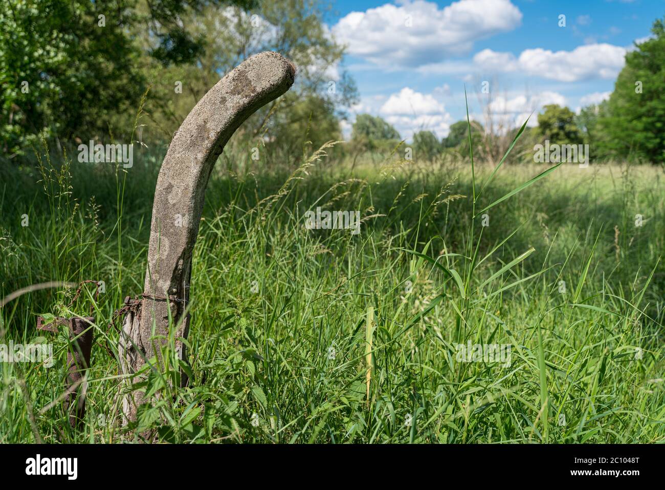 Un palo di recinzione in cemento nei prati vicino al fiume in una bella giornata estiva. Foto Stock