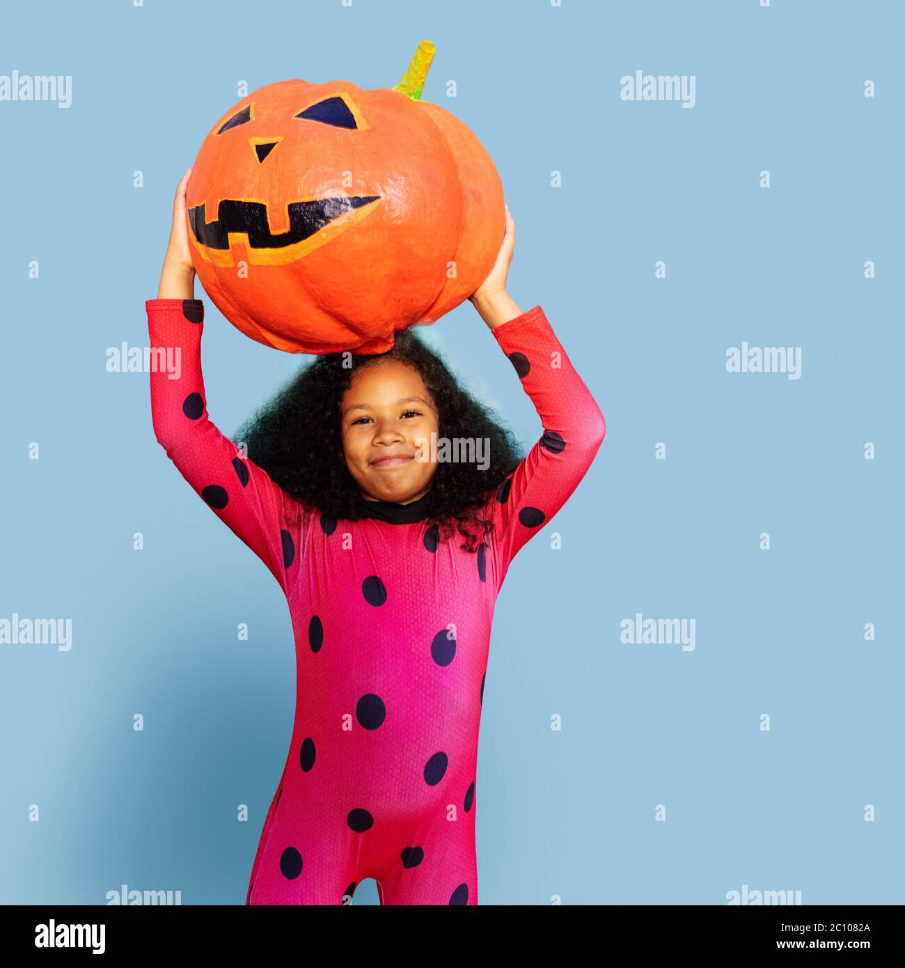 Ritratto di sorridente felice ragazza tenere Halloween zucca e sorridere sulla parete blu Foto Stock