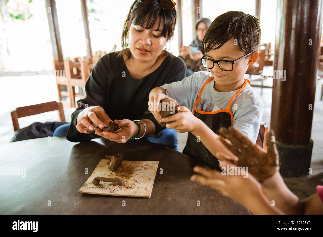 ragazzo indossa un grembiule quando gioca in argilla con sua madre in un laboratorio di galleria Foto Stock