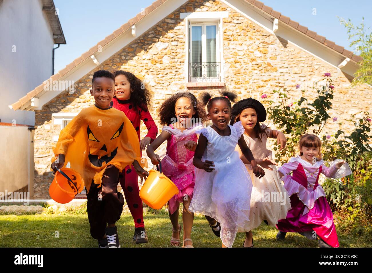 Ritratto di un gruppo di bambini che corrono in costume di Halloween sul prato prima della casa insieme, urlando con secchi caramelle Foto Stock