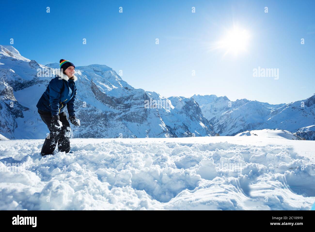 Ritratto di una ragazza giocare con neve in cappotto invernale e cappello in montagna sulla soleggiata vista di giorno da lato Foto Stock