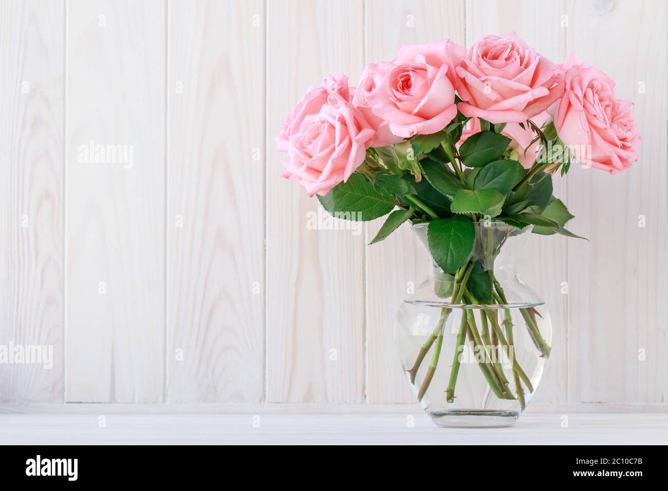 Bouquet di rose rosa in vaso di vetro su tavola di legno chiaro, sfondo floreale. Cornice festiva, carta regalo con spazio per la copia, layout floreale Foto Stock