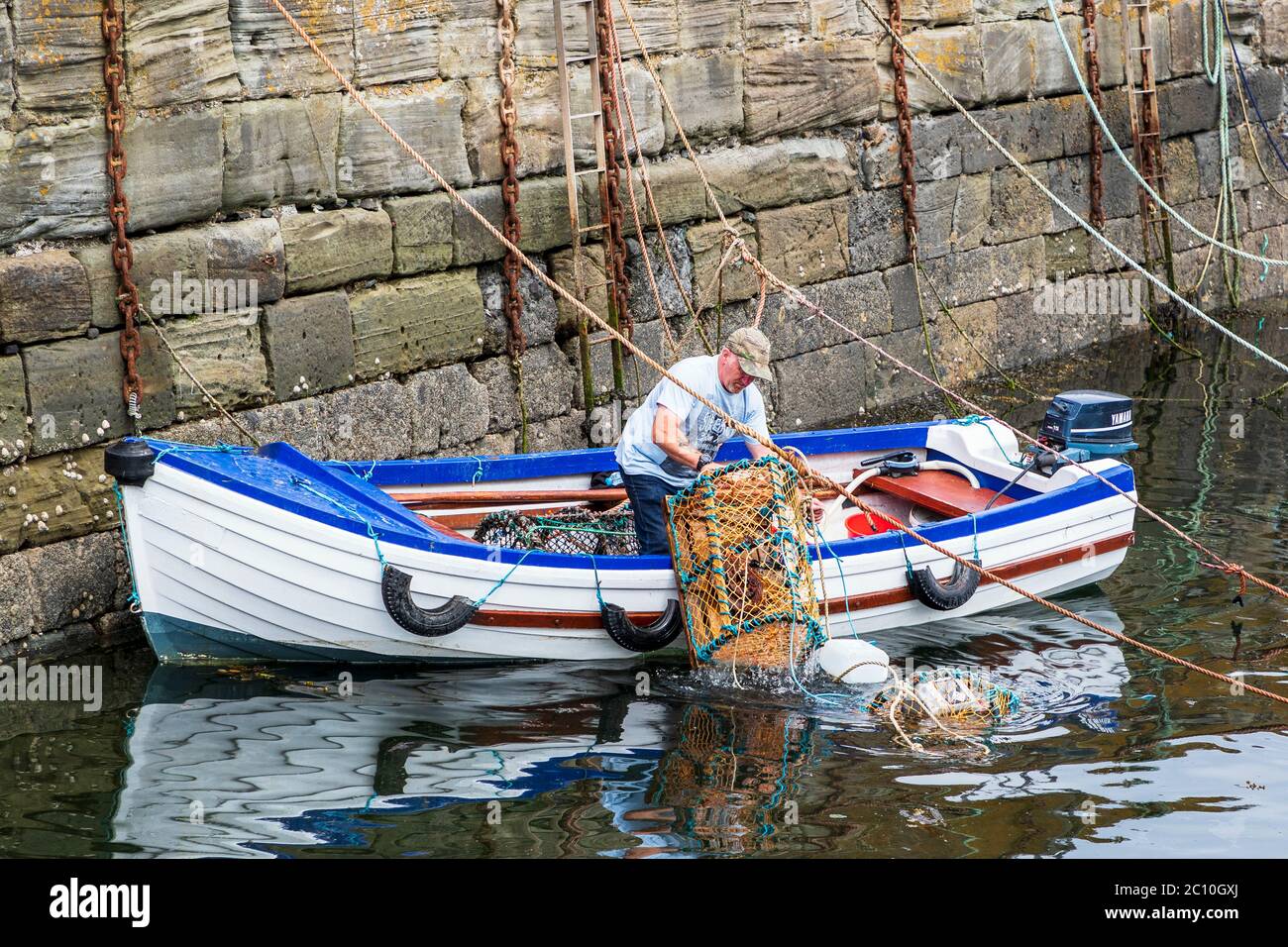 Pescatore che prepara le creelle di aragosta prima di uscire a pescare nella sua piccola barca aperta, Dunure, Ayrshire, Scozia, Regno Unito Foto Stock