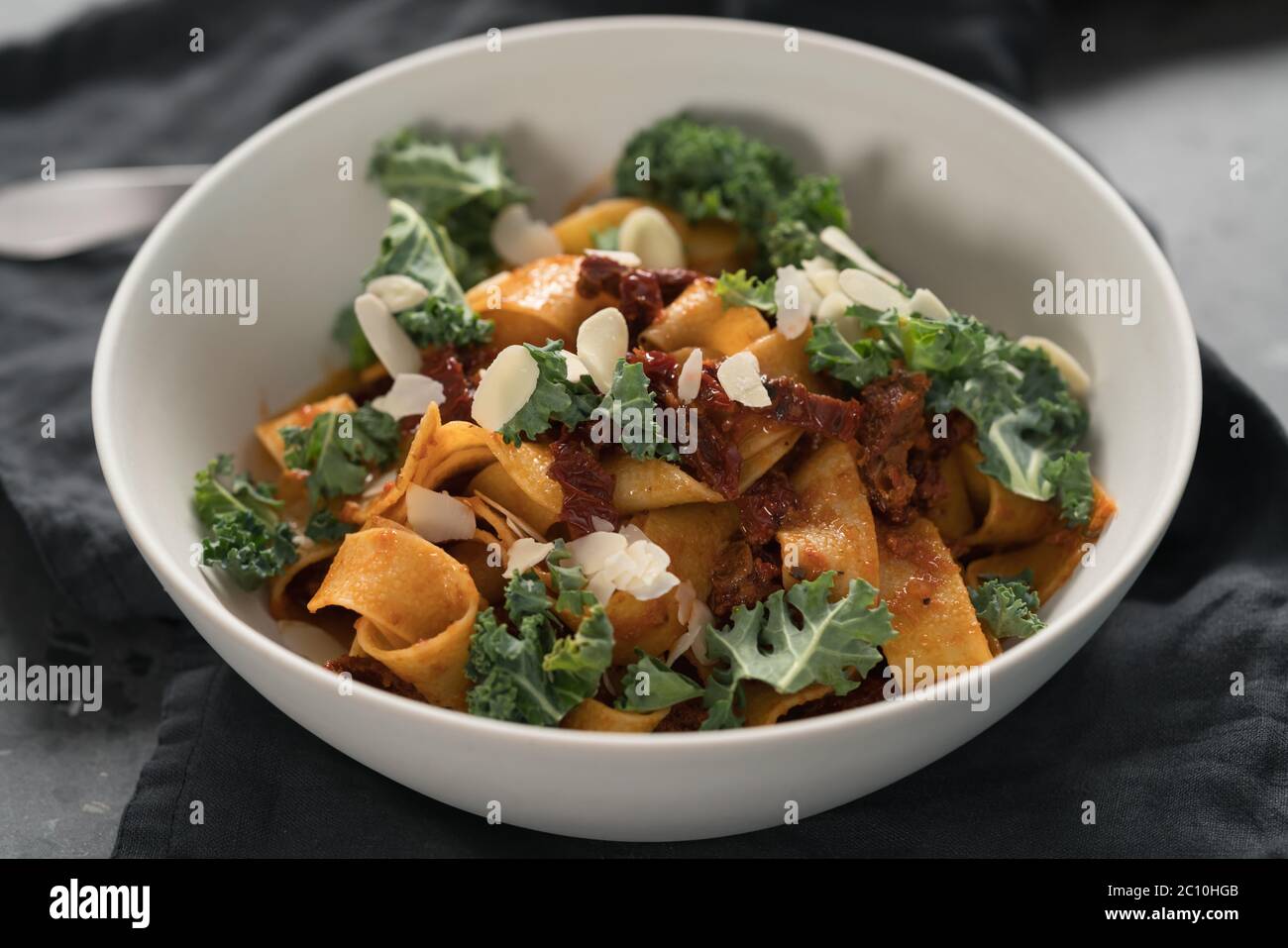 pasta di fettuccine con pomodori secchi, fiocchi di mandorle e foglie di kale, fuoco basso Foto Stock