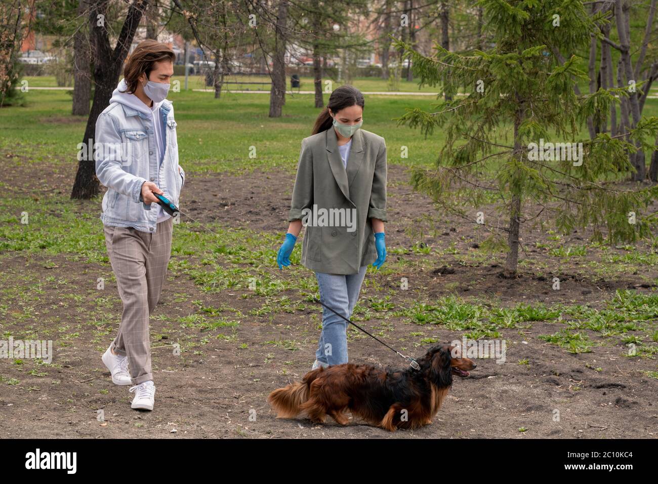 Giovane coppia in maschere di stoffa godendo di una passeggiata con il cane nel parco durante la pandemia di coronavirus Foto Stock