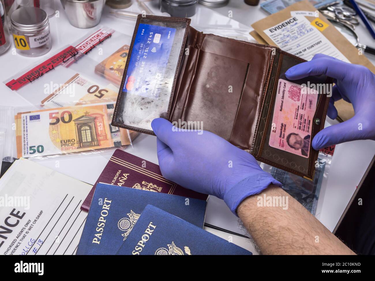 Esperto di polizia esaminando passaporto americano e portamonete di una busta di prova nel laboratorio criminalistic, immagine concettuale Foto Stock