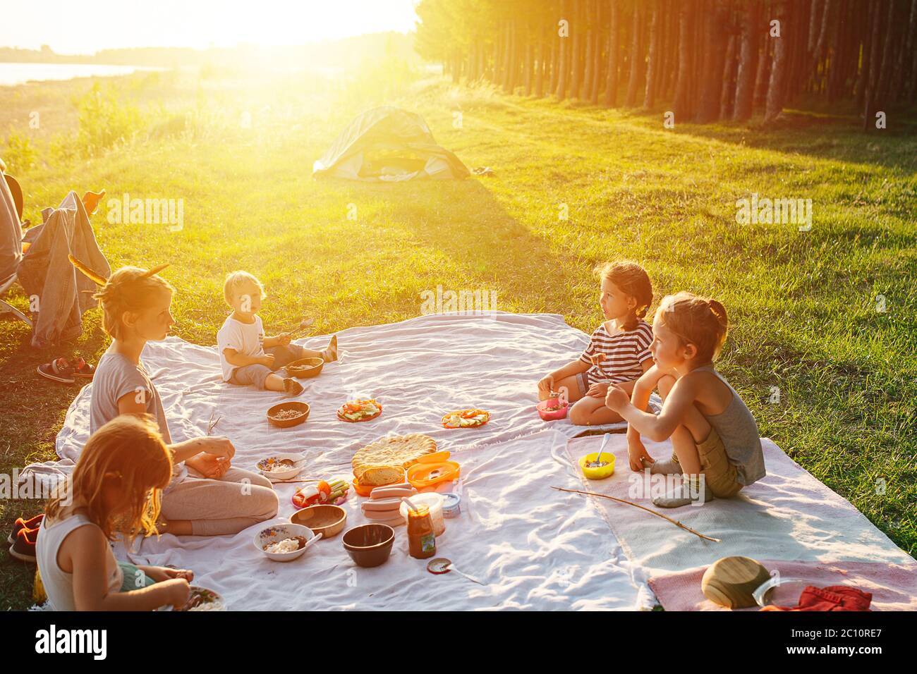 Bambini che hanno pic-nic su un prato, illuminato con un bel sole impostazione. Foto Stock