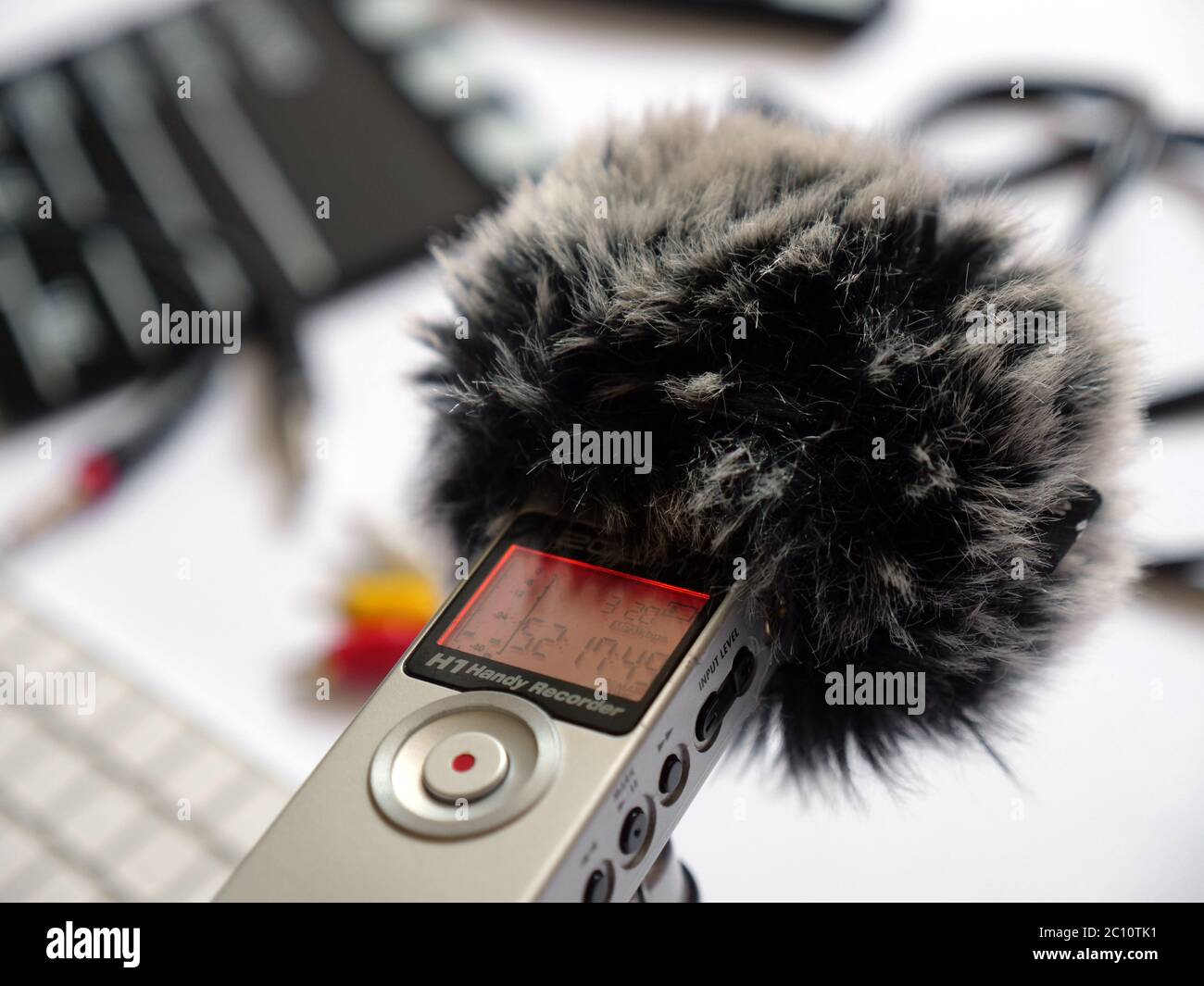 Registra l'audio all'interno di un registratore zoom h1 con un gatto morto in studio in luce naturale. Lo sfondo mostra elementi come clapperboard, tastiera, cavo, cavo, 3.5, mini jack. Puoi usare questa foto in qualsiasi progetto relativo a registrazione audio, podcast, studio di registrazione, intervista Foto Stock