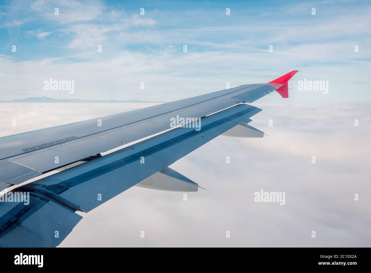 Ala di un aereo con lembi abbassati su uno sfondo di cielo blu e mare di nuvole bianche sottostanti. Foto Stock