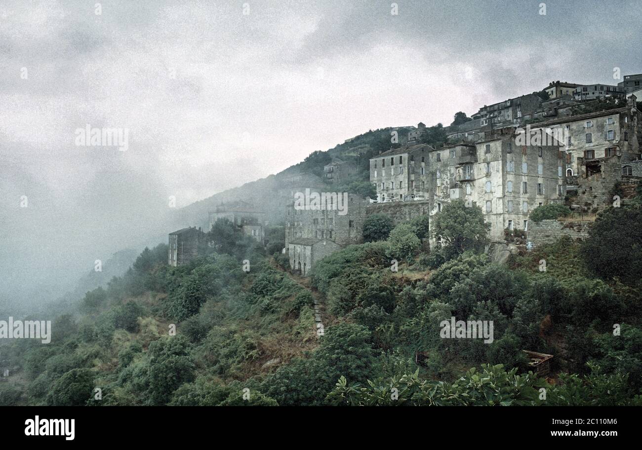 Illustrazione fotografica. Vecchie case e alberi aggrappati alla collina in una mattina nebbiosa vicino a Sartene in Corsica. 1980 Foto Stock