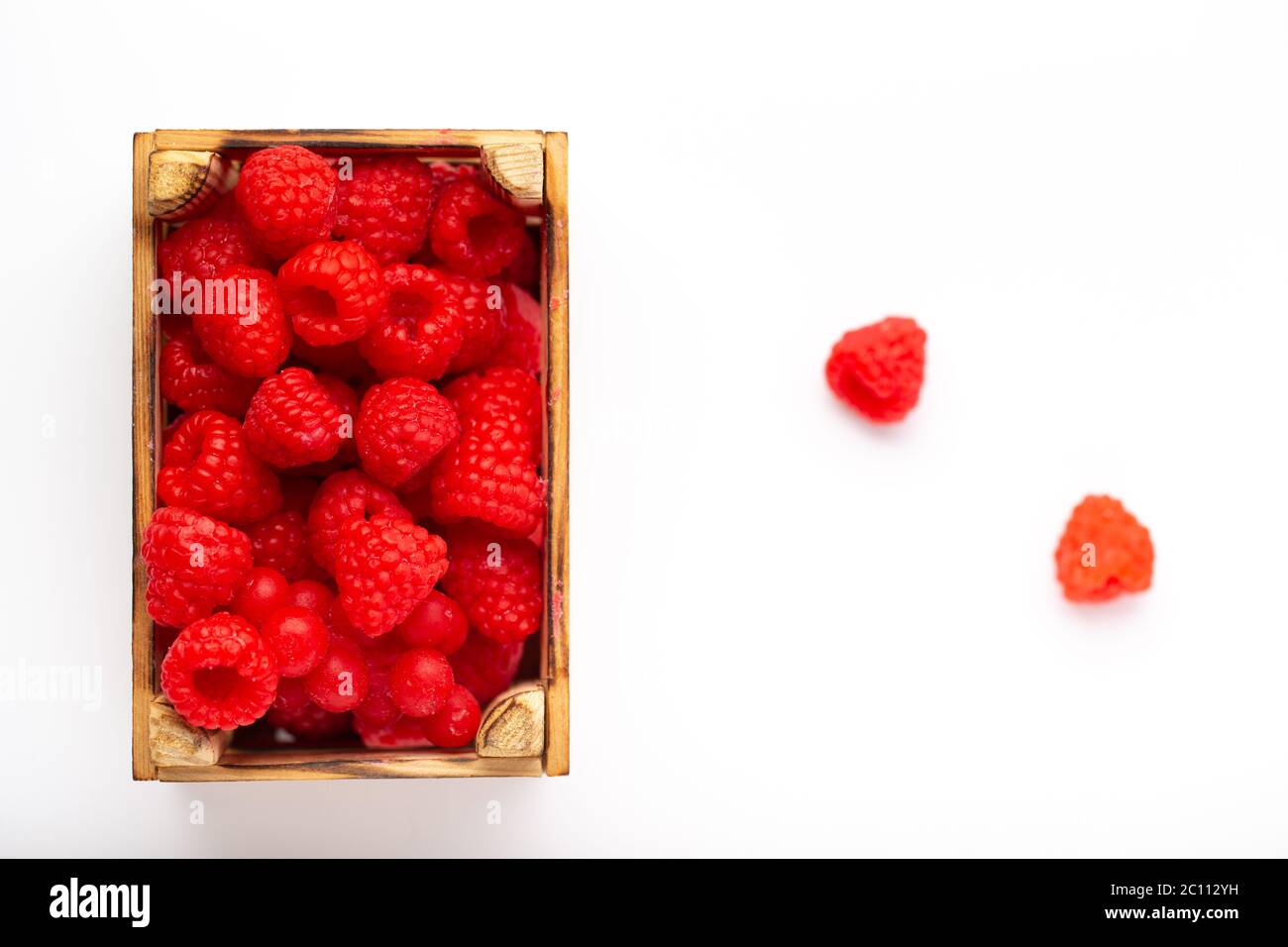 Alcuni lamponi in una piccola scatola di legno su sfondo bianco Foto Stock