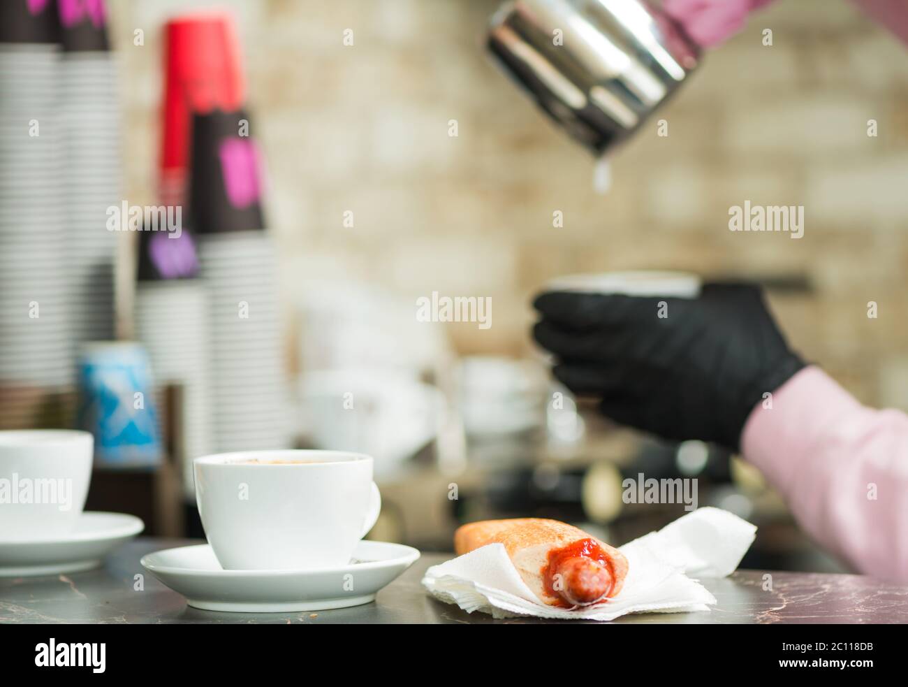 barman che versa il latte nella tazza di caffè dietro il banco del caffè Foto Stock