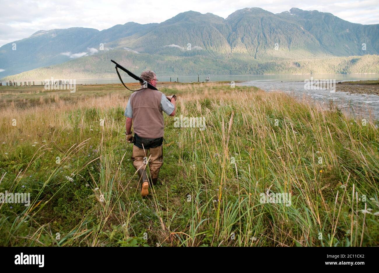 Un cacciatore che tiene una fucile e indossa i waders da pesca in un estuario del torrente nella Great Bear Rainforest, vicino a Bella Coola, British Columbia, Canada. Foto Stock