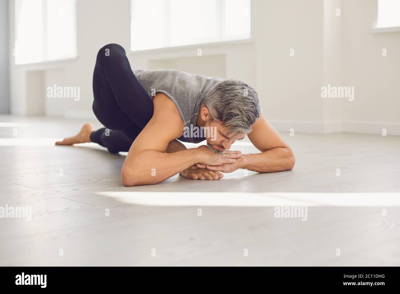 Uomo yoga. Un uomo sta praticando l'equilibrio dello yoga in una stanza grigia. Foto Stock