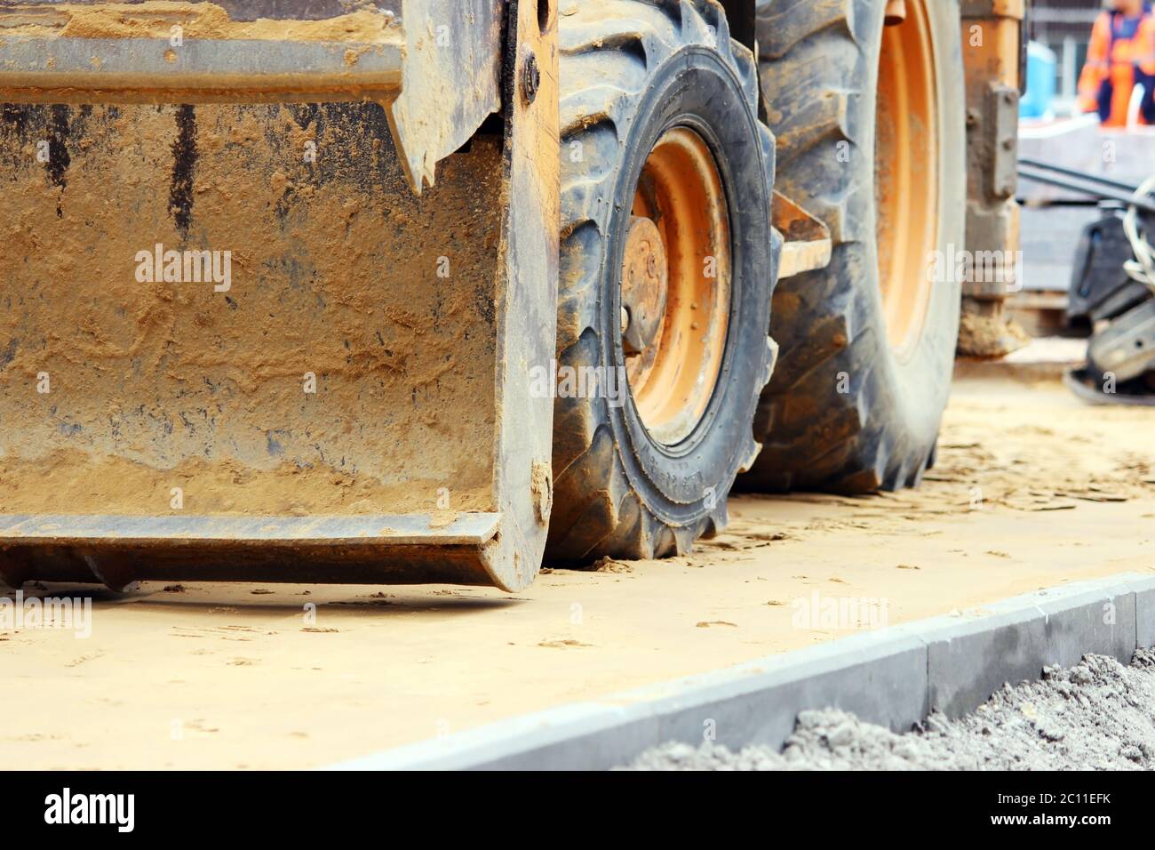 operatore di pale caricatrici sporche che lavora nella piazza della città spostando pallet di lastre di pavimentazione. Foto Stock