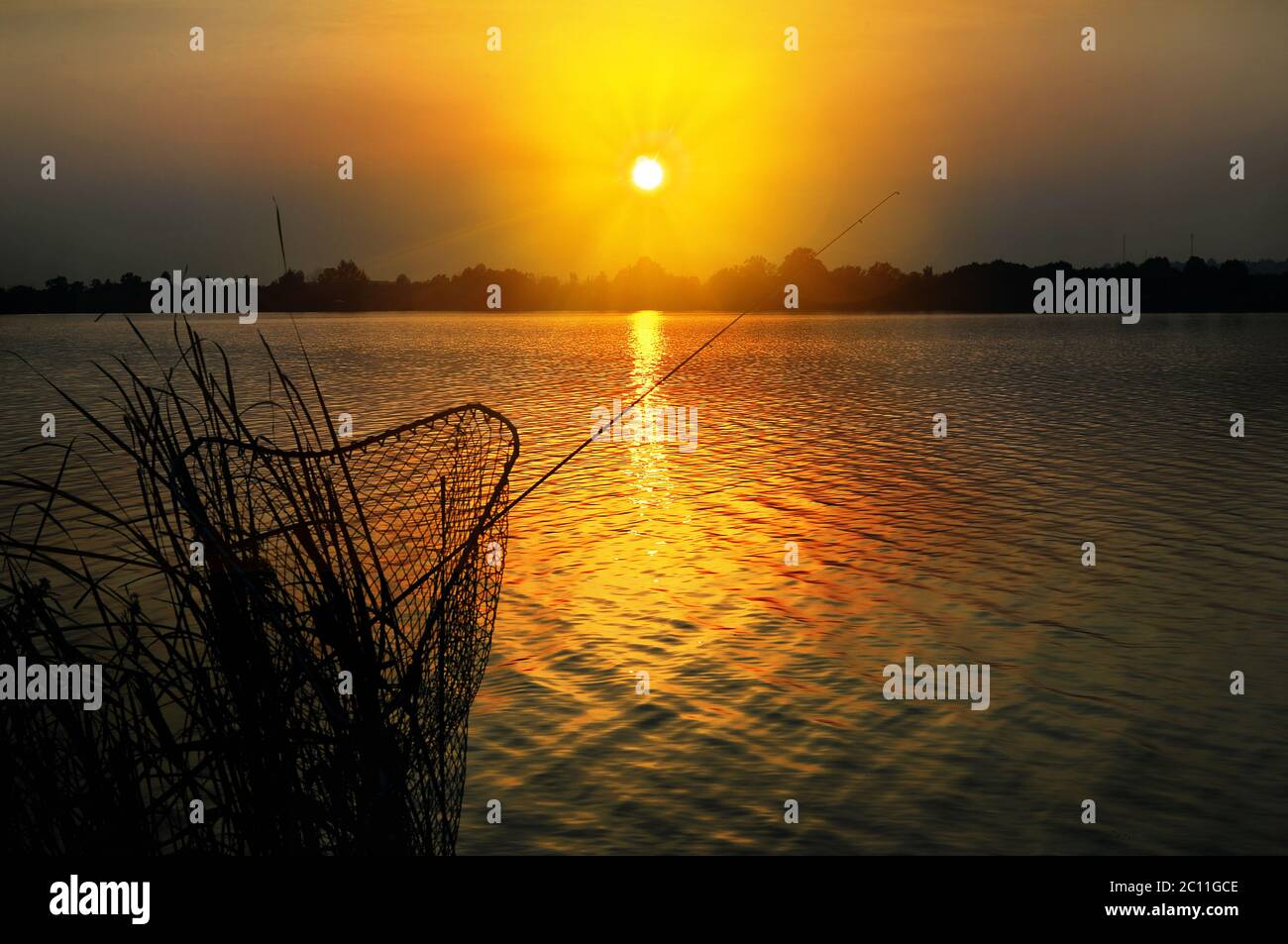 Canna da pesca e canotta contro il tramonto sul lago di pesca Foto Stock