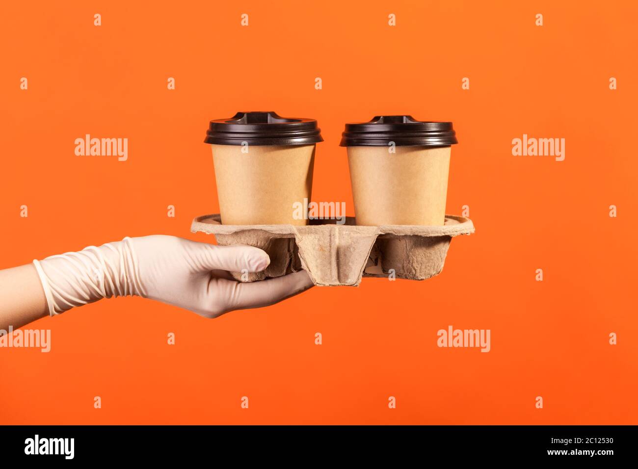 Profilo Vista laterale primo piano della mano umana in guanti chirurgici bianchi che tengono in mano e mostrano una tazza di tazza da takeaway calda. Interno, studio shot, isola Foto Stock