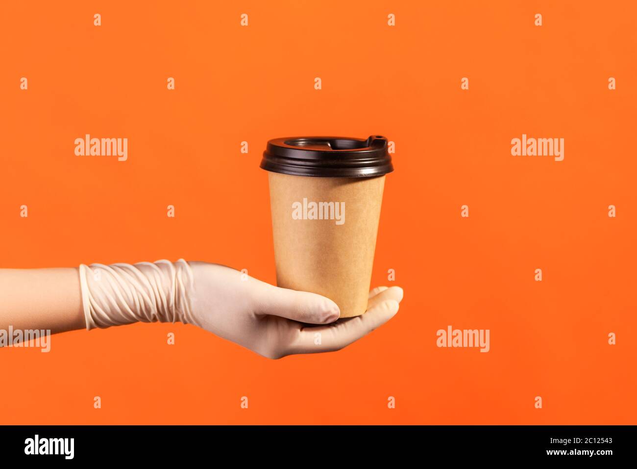 Profilo Vista laterale primo piano della mano umana in guanti chirurgici bianchi che tengono in mano e mostrano una tazza di tazza da takeaway calda. Interno, studio shot, isola Foto Stock