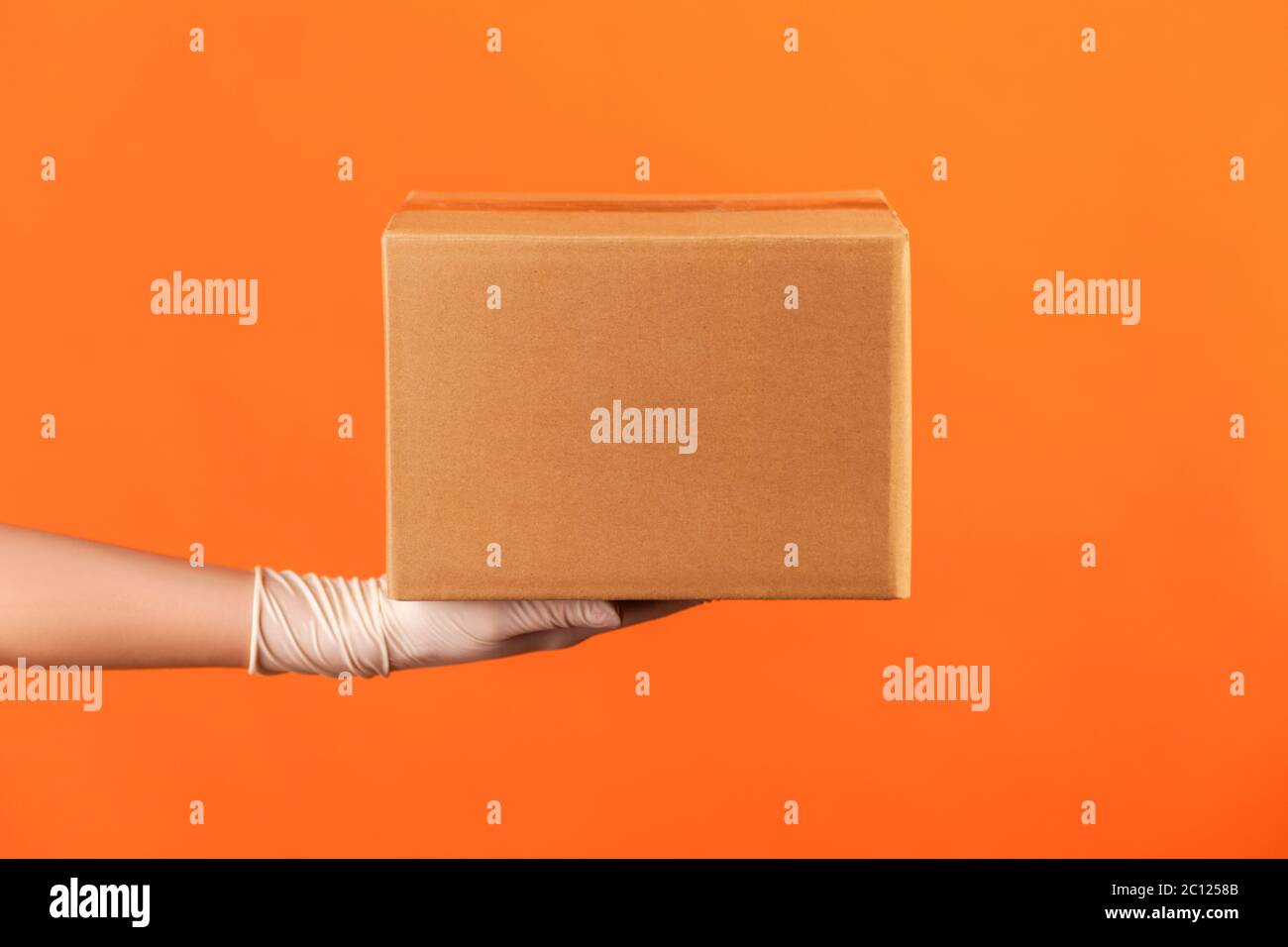 Profilo Vista laterale primo piano della mano umana in scatola di guanti chirurgici bianchi. Concetto di consegna. Interno, studio shot, isolato su sfondo arancione. Foto Stock