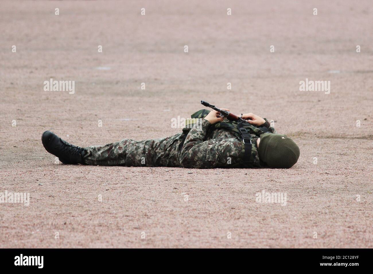Uomo in camuffamento militare abbigliamento e una maschera che si trova sulla schiena la sabbia con mitragliatrici in mano durante la dimostrazione Foto Stock