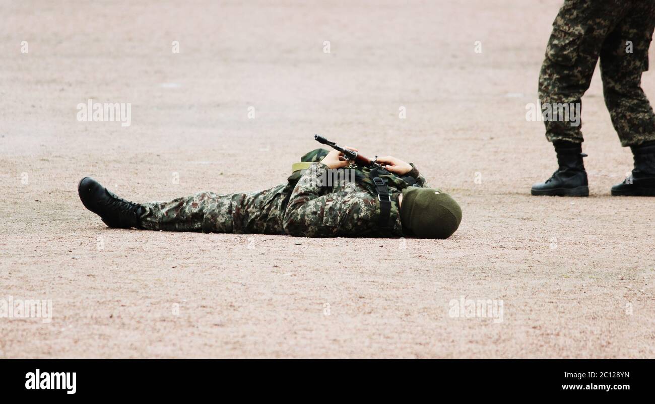Uomo in camuffamento militare abbigliamento e una maschera che si trova sulla schiena la sabbia con mitragliatrici in mano durante la dimostrazione Foto Stock