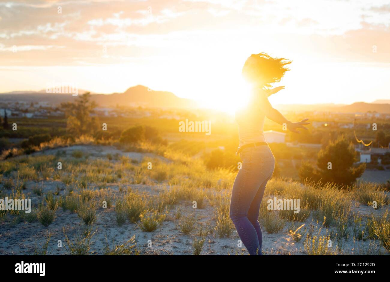Giovane donna attraente che gira a braccia aperte sulla cima della montagna contro il tramonto. Carino caldo ragazza improvvisa e godere di fredoom in natura mentre sorridendo e. Foto Stock