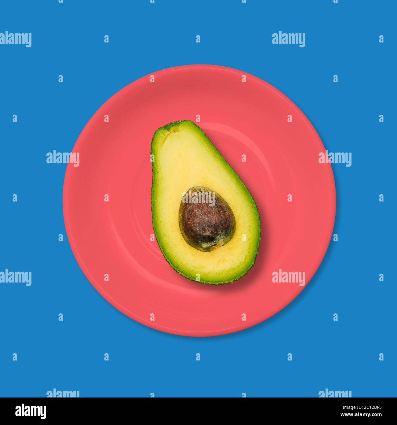 Avocado in un piatto rosso su sfondo blu. Il concetto di cibo vegetariano. Design minimalista Art. Foto Stock