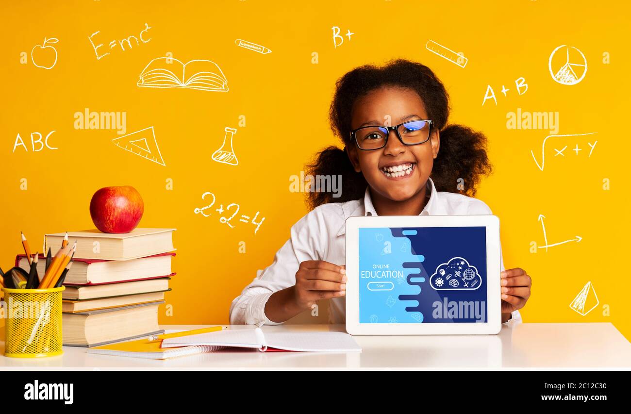 Concetto di istruzione. Ragazza che mostra tablet, seduto alla scrivania su sfondo giallo, intorno a formule e simboli scientifici Foto Stock