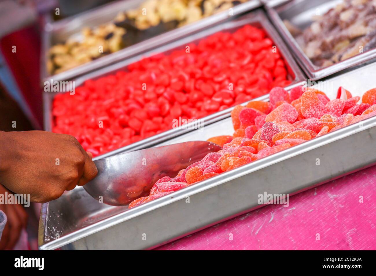 Un individuo con un cucchiaio al buffet che serve da un colorato piatto di caramelle Foto Stock
