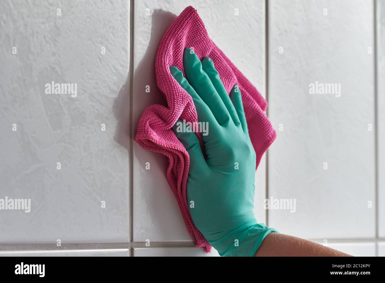 Primo piano della mano femminile con guanto e panno in microfibra per la pulizia delle piastrelle bianche del bagno Foto Stock