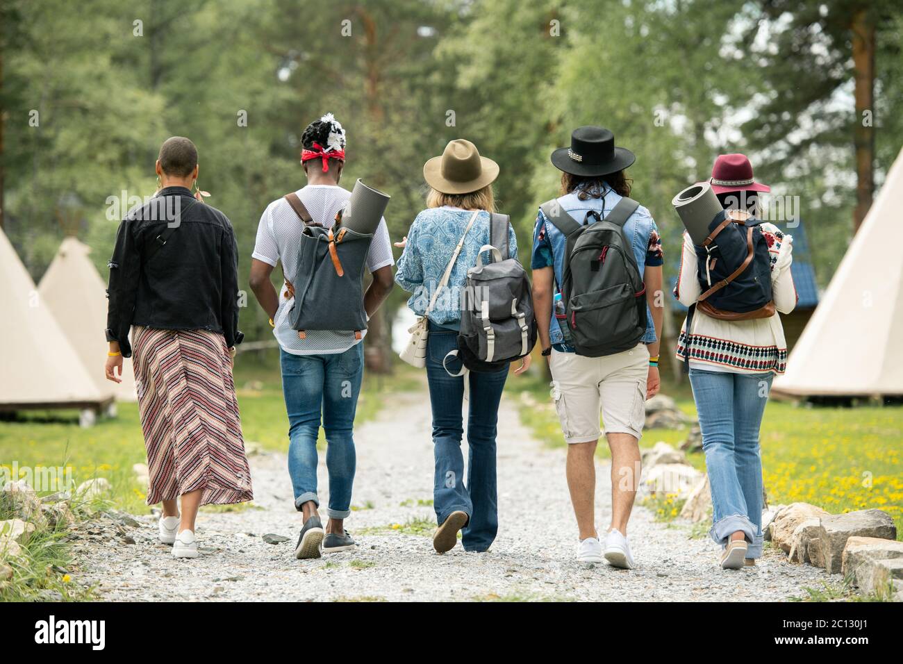 Vista posteriore dei giovani con le borse a mano che camminano sul campeggio del festival mentre si trova la tenda Foto Stock
